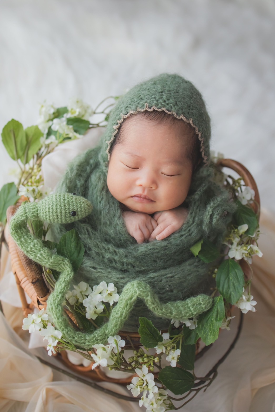 白い花と緑のニットに包まれてかごで眠る新生児